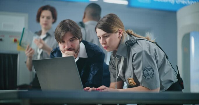 Airport Security Checkpoint: Two Diverse TSA Workers Using Laptop, Discussing Security Issues. Transportation Security Administration for Travel Safety. In the Background, Airport Staff Working.