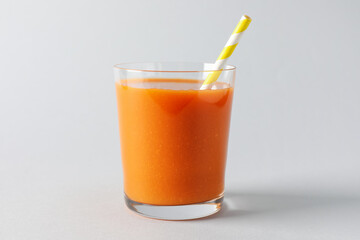 Fresh carrot smoothie in glass on light grey background, closeup