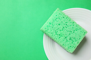 Plate with sponge on green background, top view. Space for text