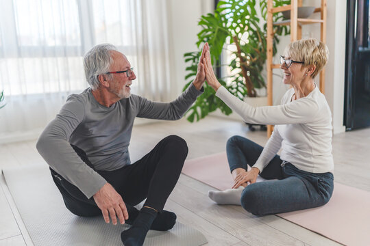 A happy senior couple sitting on yoga mats at home, giving each other a high-five after completing a workout, celebrating fitness, health, and togetherness - Powered by Adobe