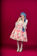 Cosplayer wearing sweet lolita fashion covering her mouth with hands on pink background