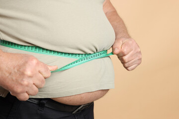 Overweight man measuring his belly with tape on beige background, closeup