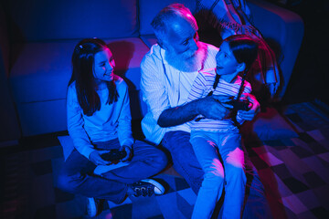 Fototapeta premium Grandfather playing video games with grandchildren in cozy room under colorful lighting, bonding and sharing joyful family moments.