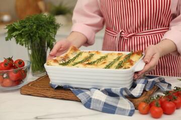 Woman putting baking dish with tasty lasagna onto white marble table indoors, closeup