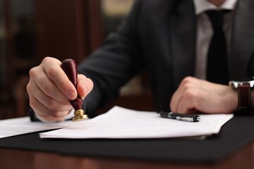 Notary stamping document at table in office, selective focus