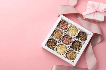 Flower shaped chocolate bonbons in box, gift and ribbon on pink background, flat lay. Space for text