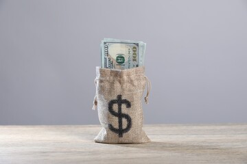 Dollar banknotes in burlap sack on wooden table against grey background