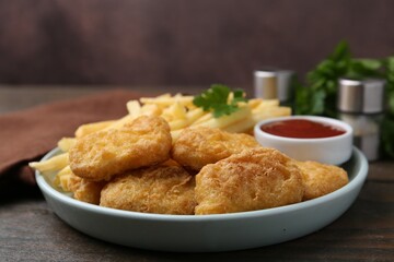 Tasty chicken nuggets and french fries with sauce on wooden table, closeup