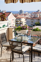 Glass table with wicker chairs on a hotel terrace with flowering flowerpots on the railings
