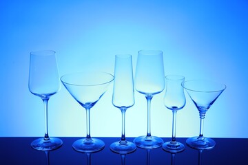 Many empty clean glasses on mirror surface against blue background