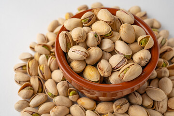 Salted pistachios in a glass bowl and scattered around on a white background, isolated, side view, crunchy roasted nuts,tasty,nutritious snack, healthy organic food, high-protein vegetarian ingredient