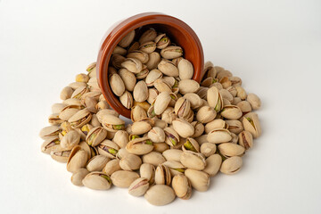 Salted pistachios pouring out of a glass bowl on a white background, isolated, side view, crunchy roasted nuts, tasty and nutritious snack, healthy organic food, high-protein vegetarian ingredient