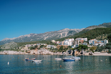 Obraz premium Fishing boats are moored in the sea near colorful hotels on a rocky slope. Przno, Montenegro