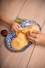 Manos compartiendo una empanada rellena de pollo y maíz
