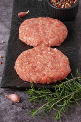 Fresh ground meat patty ready for cooking with herbs and garlic on a dark plate