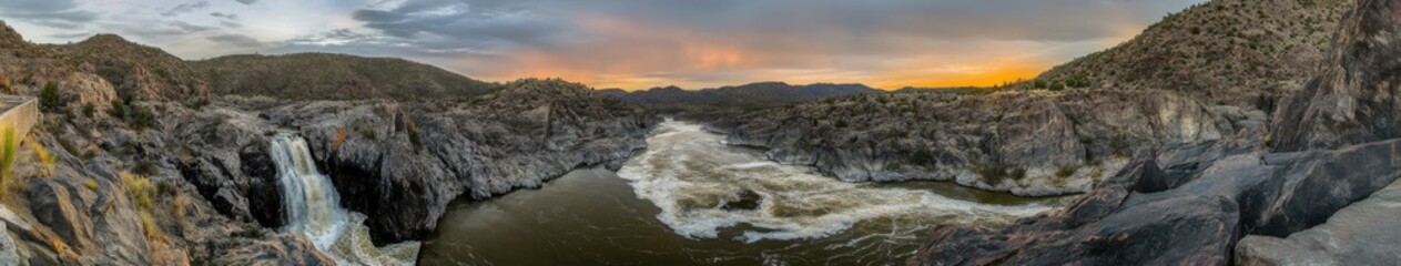 Fototapeta premium Panoramic view of a mountain river flowing through rugged terrain during sunset with vibrant colors in the sky