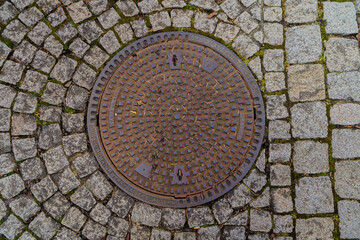 Round metal manhole cover on a cobblestone pavement. Urban detail, infrastructure. Close-up, top view
