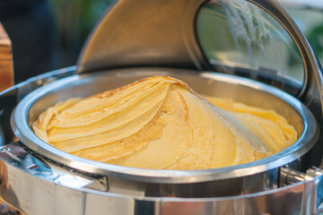 Image depicts a stainless steel griddlepan with transparent lid, cooking pancakes
