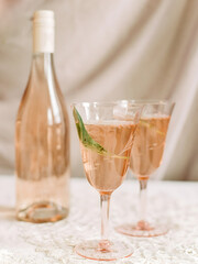 Stylish glasses of pink cocktail beside a bottle on a white table with elegant background in a cozy setting
