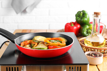 Frying pan with vegetables and stove on wooden table indoors, closeup
