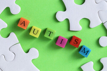 Obraz premium Word Autism made with colorful cubes and puzzle pieces on green background, flat lay