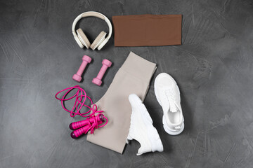 Stylish sportswear, dumbbells, white sneakers, skipping rope and headphones on grey background, flat lay