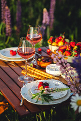Beautiful romantic outdoor wedding decor in a field. Table decorated with purple lupines flowers. Wineglasses with white wine. Sunset, summer, golden hour. Perfect surprise date for loving couple