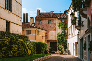 Sunlight illuminating the vibrant buildings and lush greenery of Vicolo Spineda in Treviso, Italy, creates a serene and inviting atmosphere in the charming alley