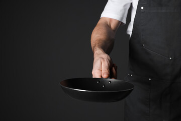 Chef holding frying pan on black background, closeup. Space for text