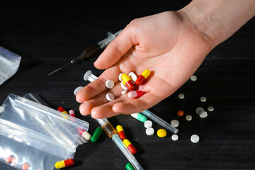 Drug addiction. Woman with pills at black wooden table, closeup
