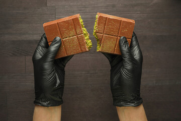 Woman breaking Dubai chocolate bar with pistachio and knafeh at wooden table, top view