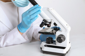 Laboratory testing. Scientist working with microscope at white marble table, closeup
