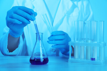 Laboratory testing. Scientist working with glassware at table, closeup. Toned in blue