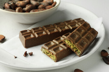 Tasty Dubai chocolate bars with pistachios, knafeh and cocoa beans on light table, closeup