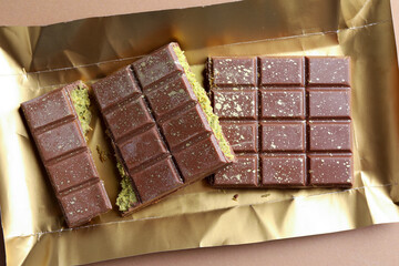 Pieces of delicious Dubai chocolate with pistachios and knafeh on dark beige background, top view