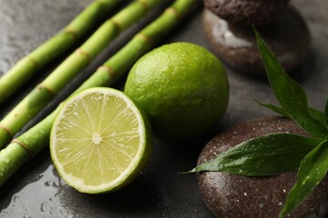 Spa composition with wet limes, pebble stones, bamboo leaves and stems on grey table, closeup