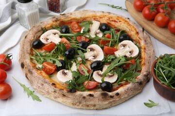 Tasty pizza with cherry tomatoes, black olives, mushrooms and arugula on white table, closeup