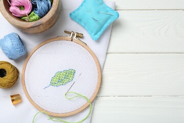 Embroidery and different sewing accessories on white wooden table, flat lay. Space for text