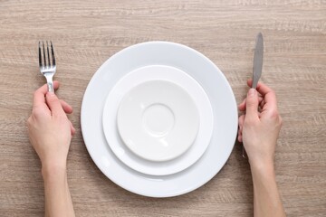 Woman with cutlery and ceramic plates at wooden table, top view