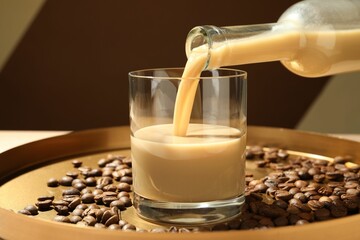 Pouring coffee cream liqueur in glass at table, closeup