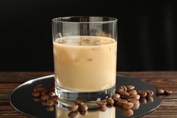 Coffee cream liqueur in glass and beans on wooden table, closeup