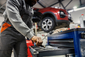 Close up of interracial repairman's hand taking tool and preparing for car fixing at auto mechanic...