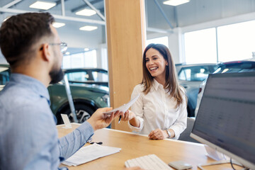 Smiling car buyer giving contract to salesman at car showroom.