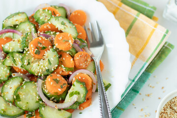 Cucumber carrot salad with sesame seeds in a plate with fork. Top view. Close-up.