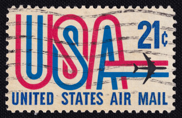 Old vintage cancelled postage stamp of the United States of America with the image of airmail, airplane and the inscription USA close-up. Macro image of the stamp on a black background.