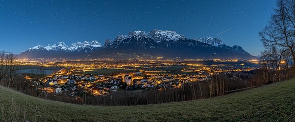Night panorama of illuminated village nestled in valley, majestic snow-capped mountains in background under starry sky.