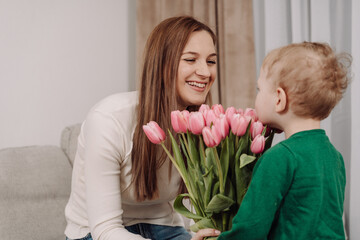 A smiling mother receives a bouquet of pink tulips from her young child. A touching moment of love...