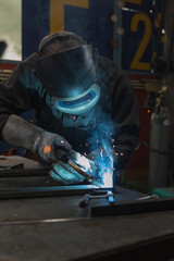 Skilled welder worker with experience in metal fabrication, using MIG welding techniques to create sparks and shape metal components.
