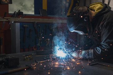 Seasoned skilled blue-collar worker working in a workshop creating sparks while welding metal...