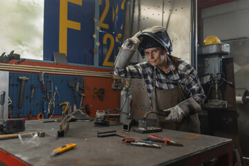 Female welder in face shield welding metal in workshop while sparks flying around. Women in men's...